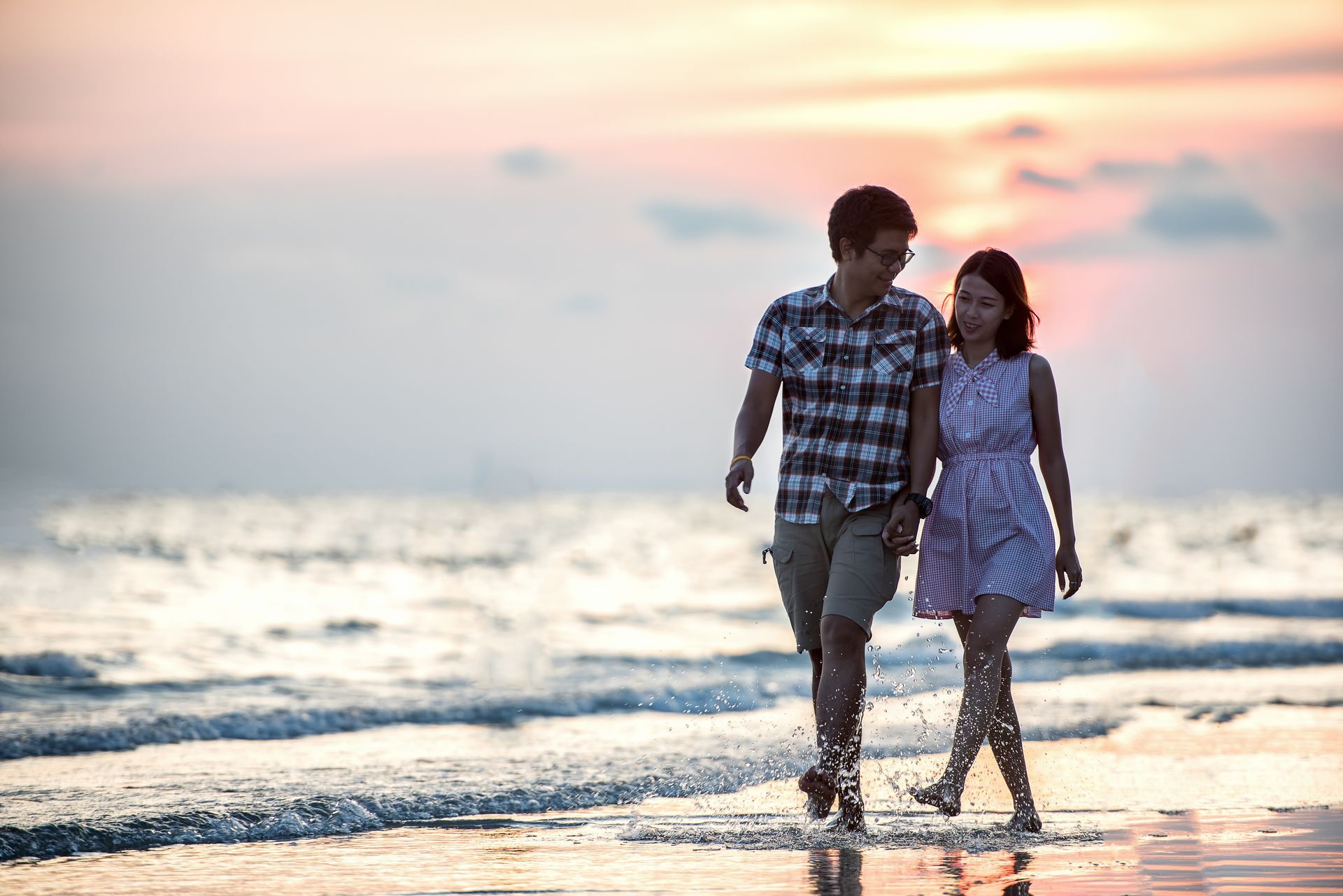 Two people walking hand in hand along a beach at sunset