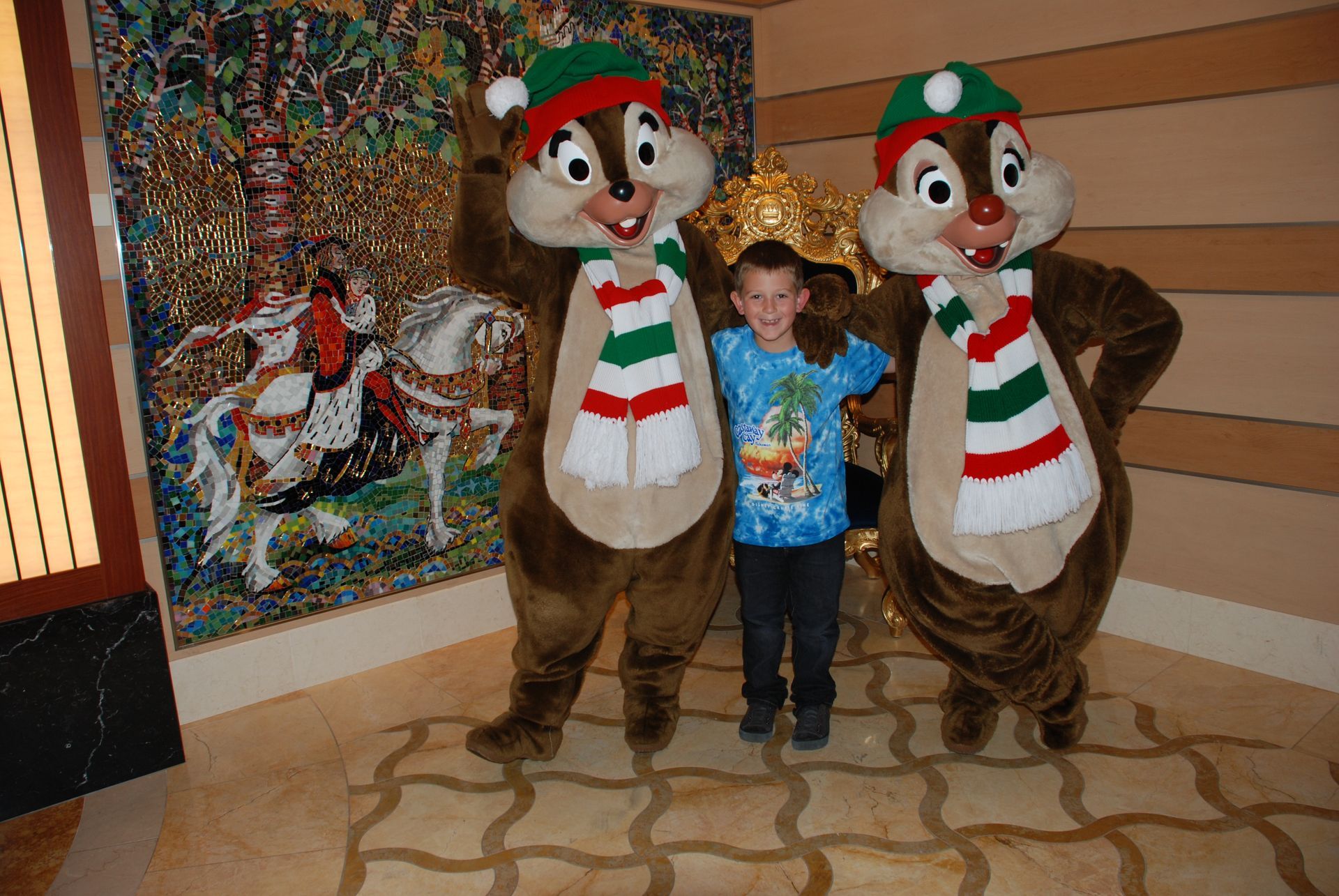 Child posing with two holiday-costumed chipmunk mascots in a festive indoor setting