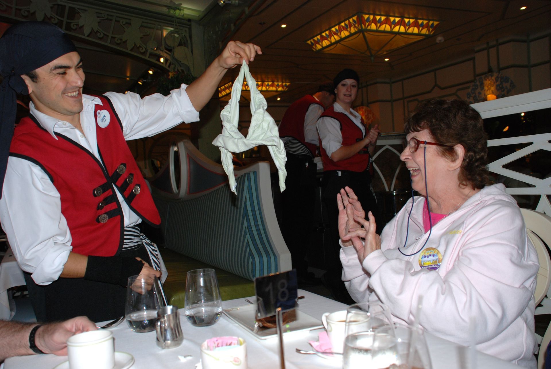 Chef in red vest presenting hanging dough to seated diner at a restaurant table