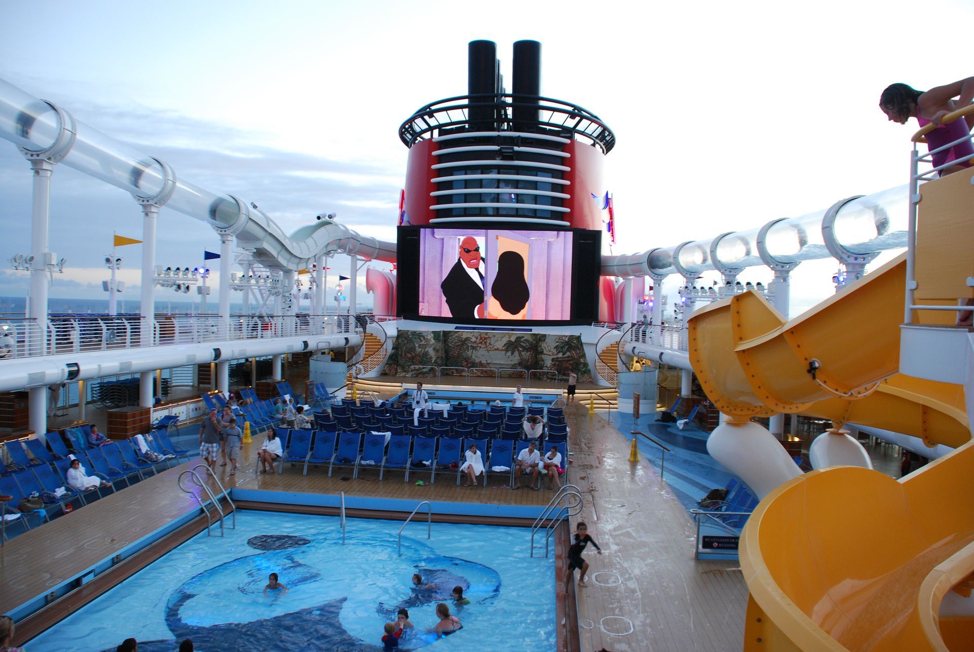 Cruise ship deck with pool, waterslides, and giant outdoor movie screen
