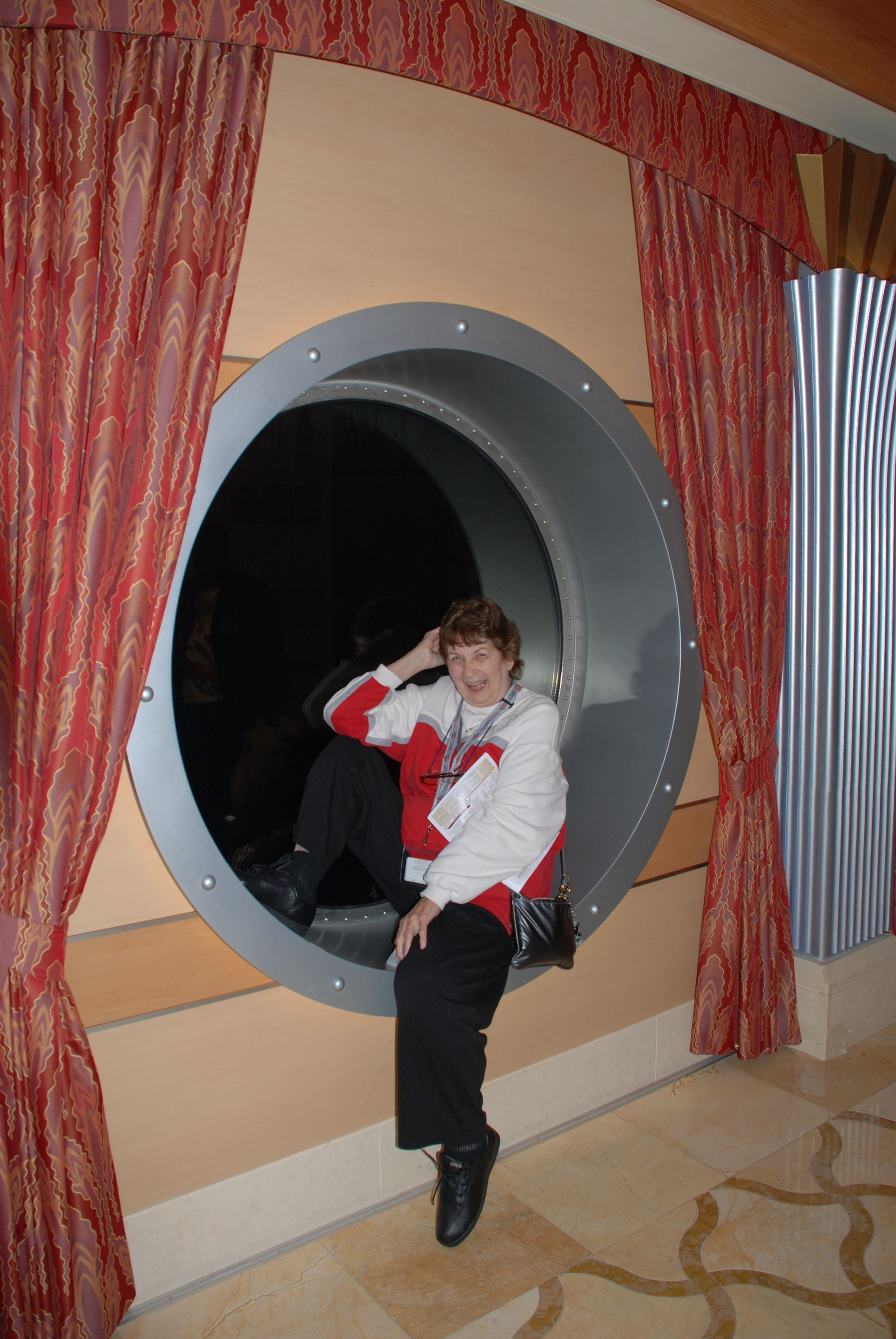 Person sitting on the edge of a large circular tunnel display, surrounded by red curtains.