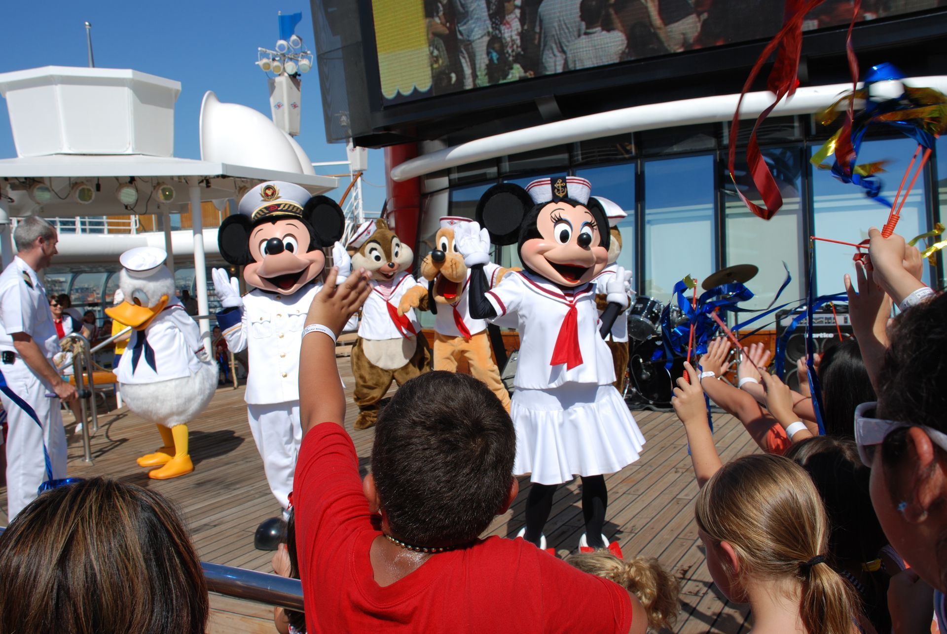 Mickey and Minnie Mouse perform on a cruise ship deck as a crowd watches and takes photos