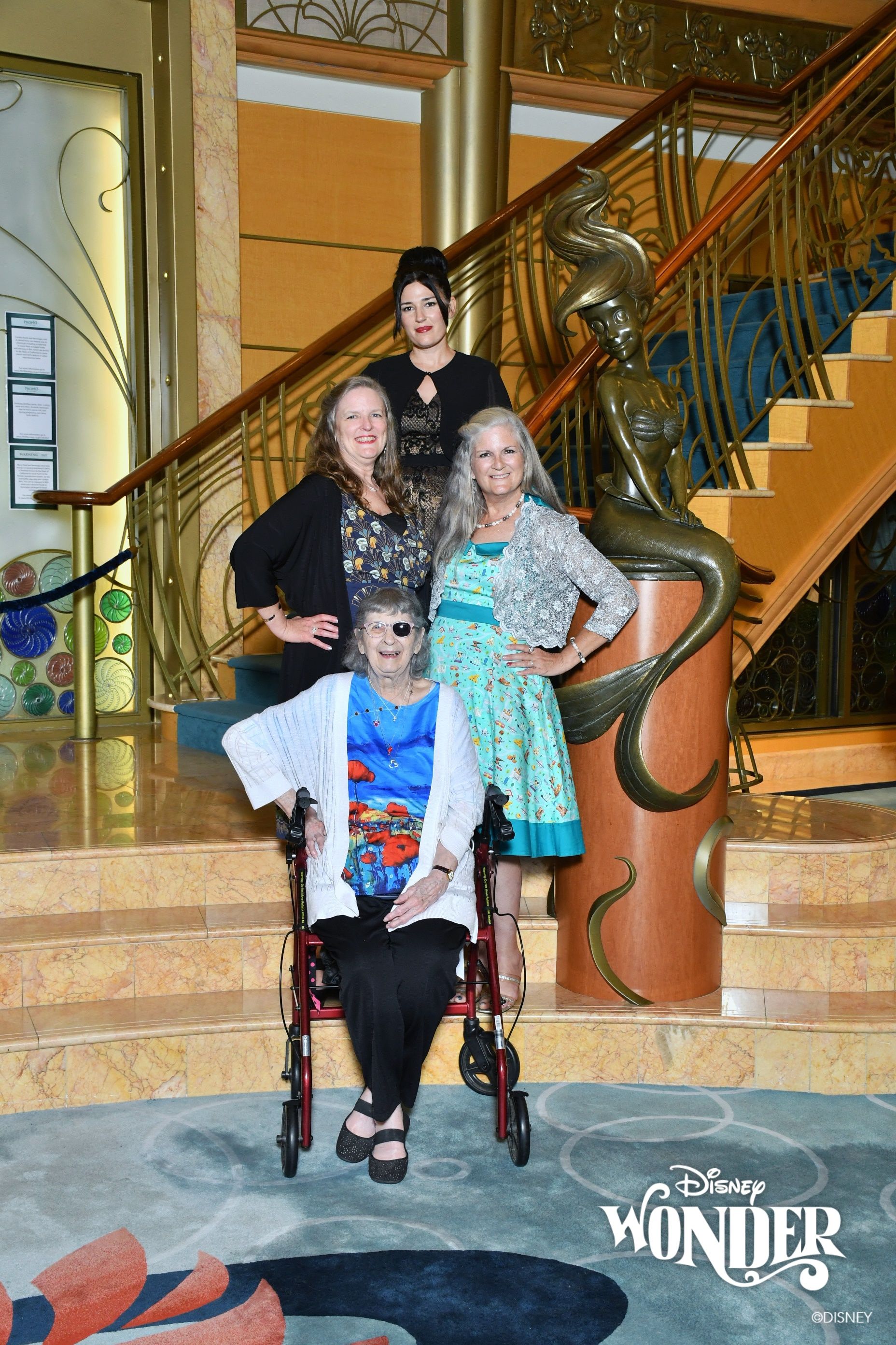 Group posing on a grand staircase in a cruise ship lobby, with a Disney Wonder logo visible at the bottom.