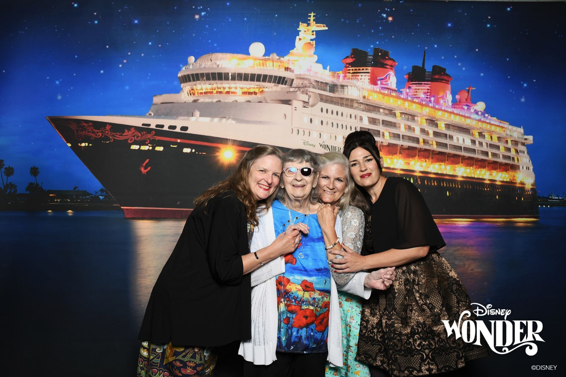 Four people posing in front of a glowing cruise ship backdrop, with “Wonder” logo at bottom right