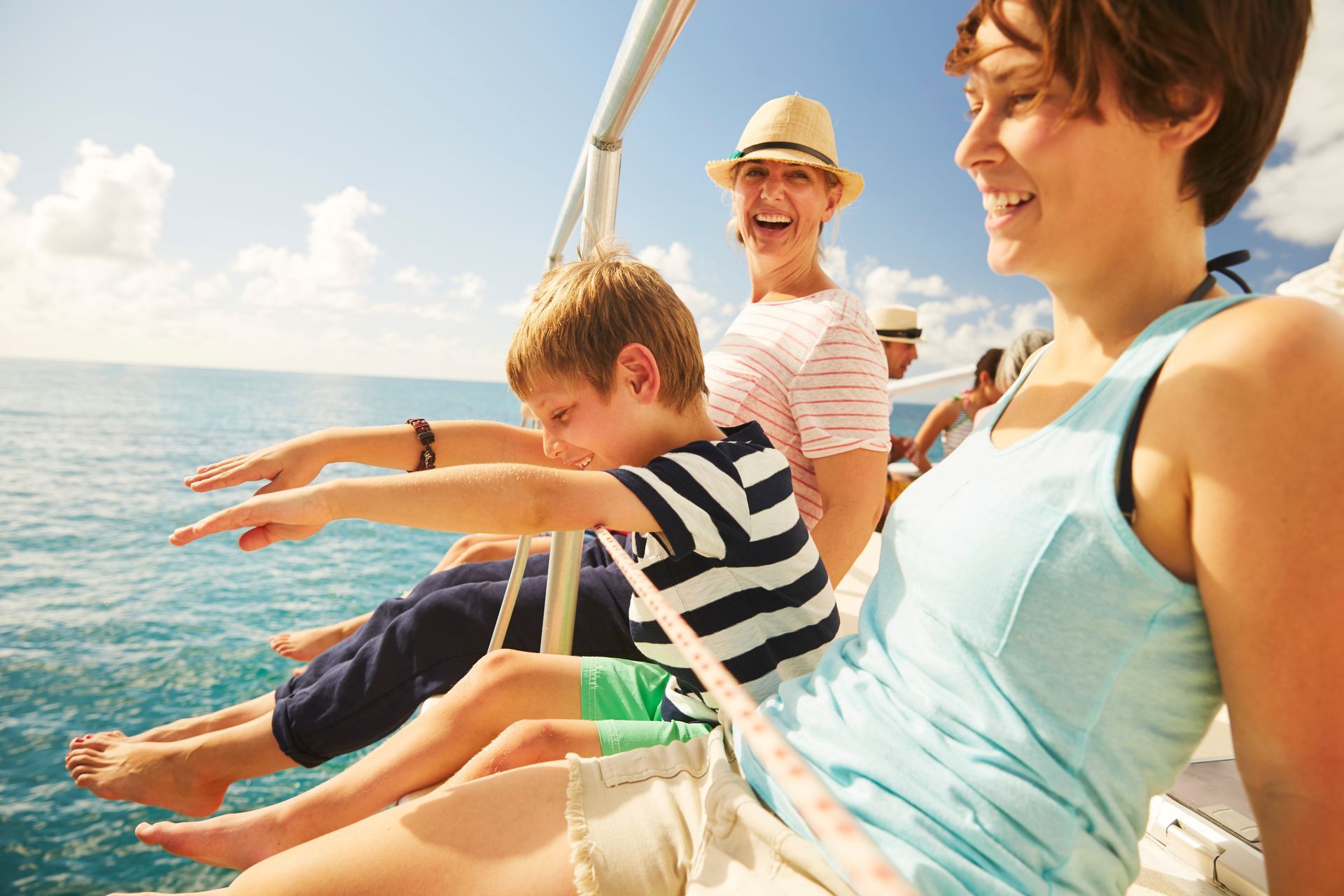 Family relaxing on a sailboat, smiling and dangling feet over the water in bright sunlight