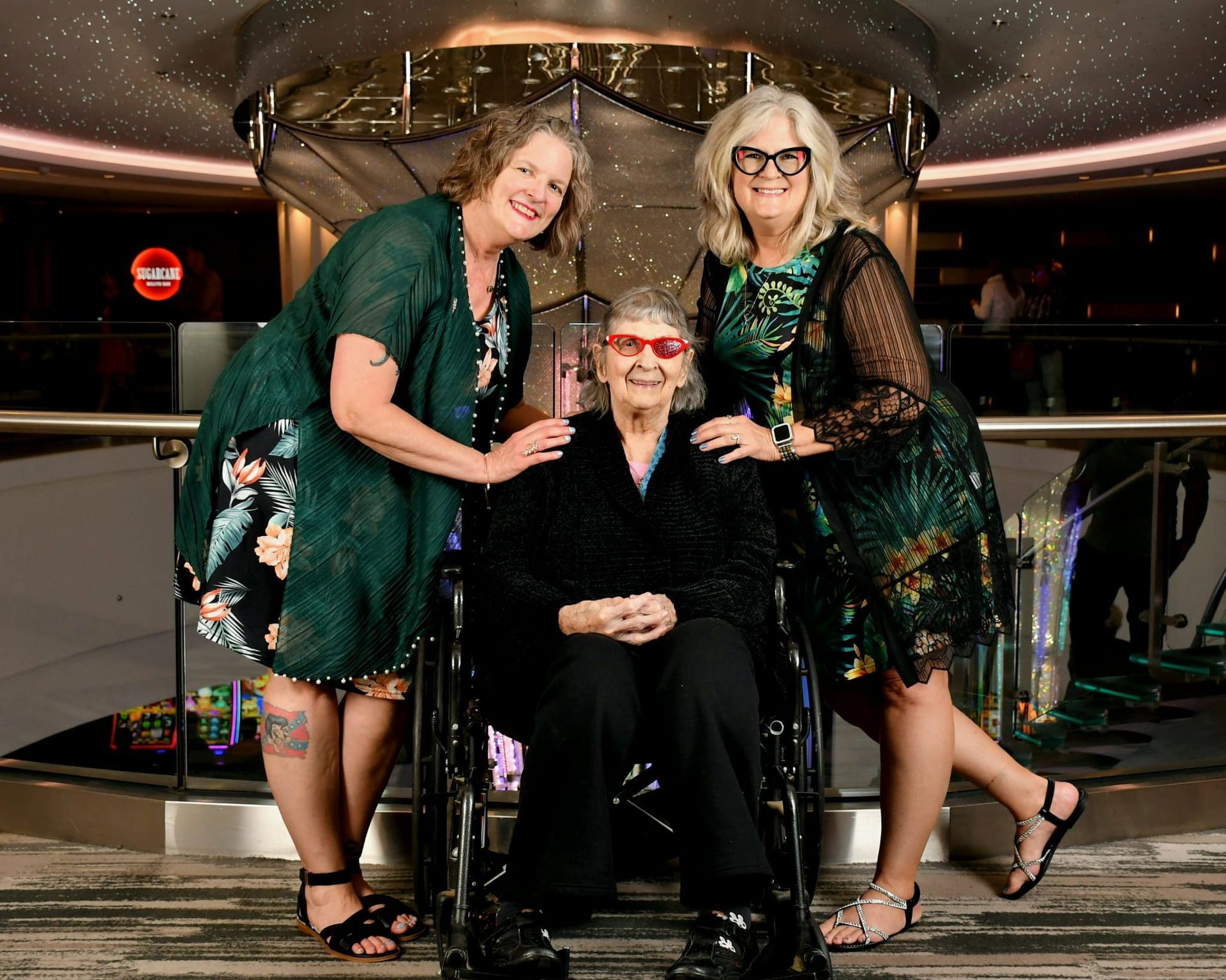 Three women in matching green dresses pose together indoors, smiling by a railing.
