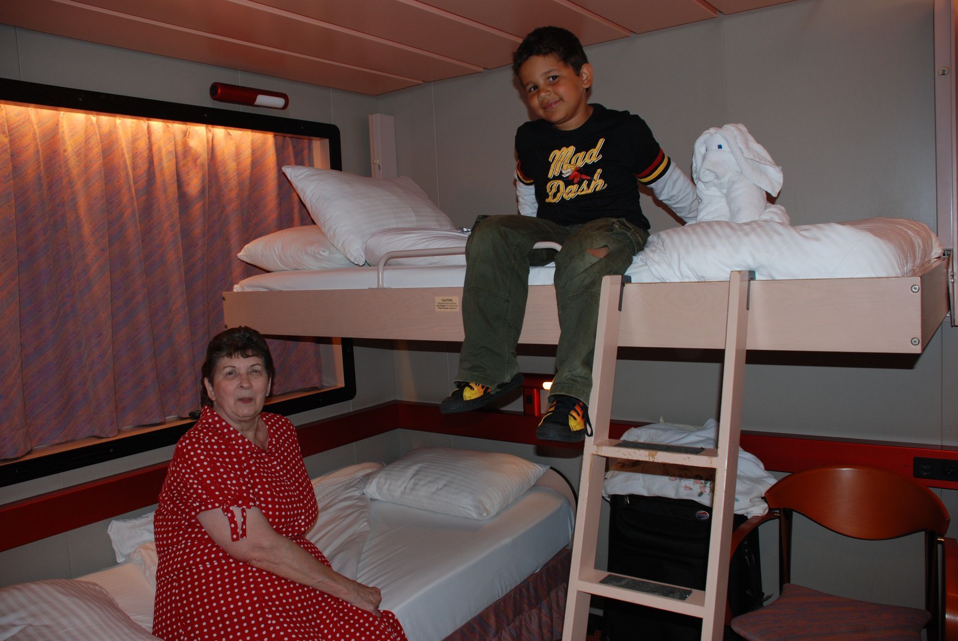 People in a bunk room: a child sits on the top bunk while another sits on the lower bed.