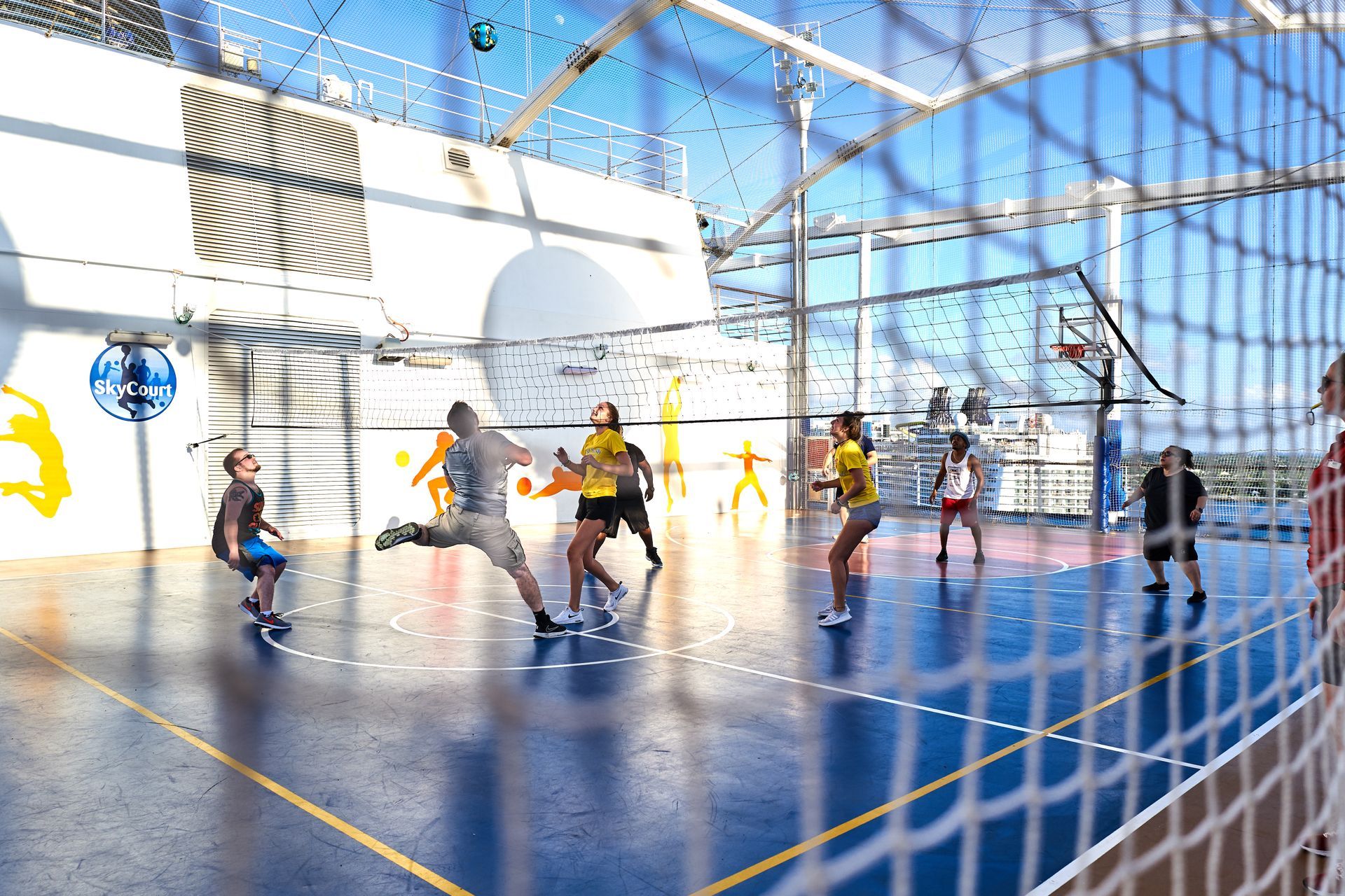People playing indoor futsal on a blue court, seen through a goal net.