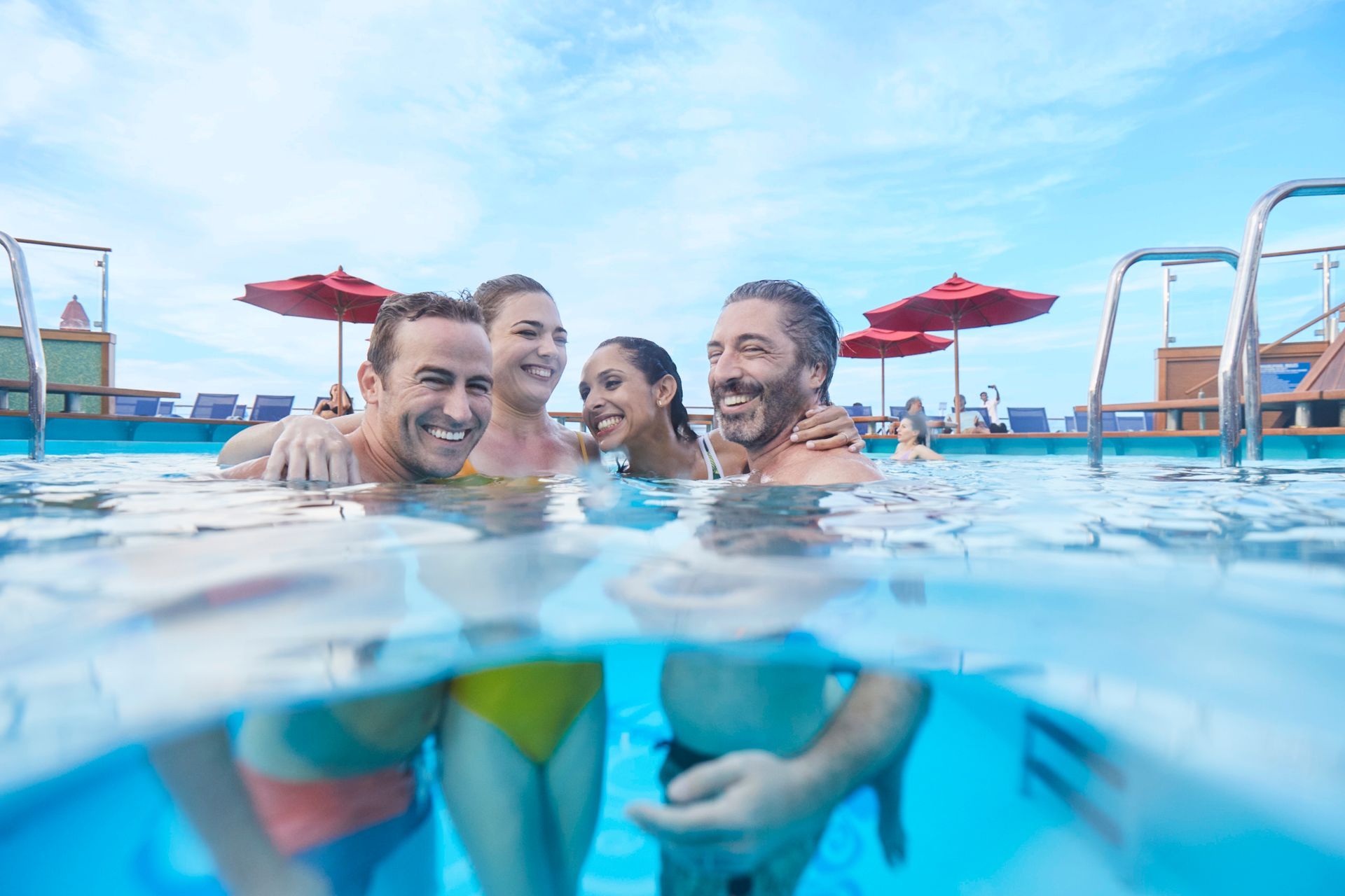 Friends smiling in a swimming pool with a red waterslide and blue sky in the background