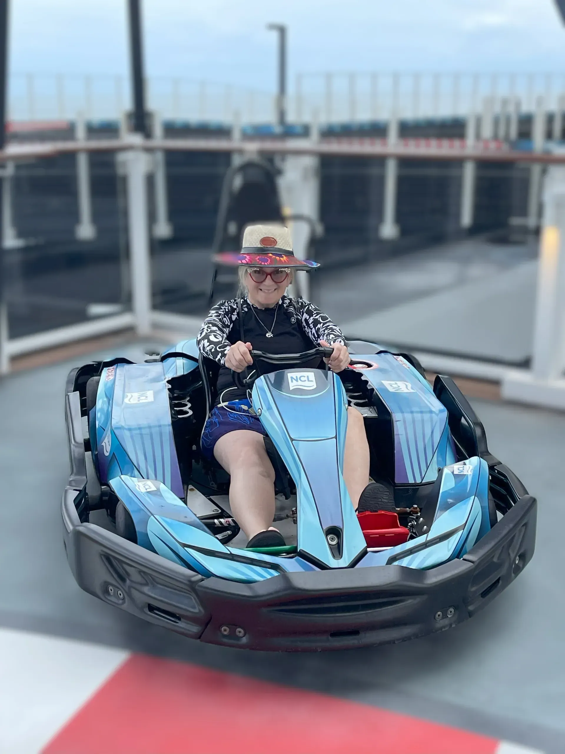 Person riding a blue bumper car on a rooftop track, wearing a straw hat and sunglasses.