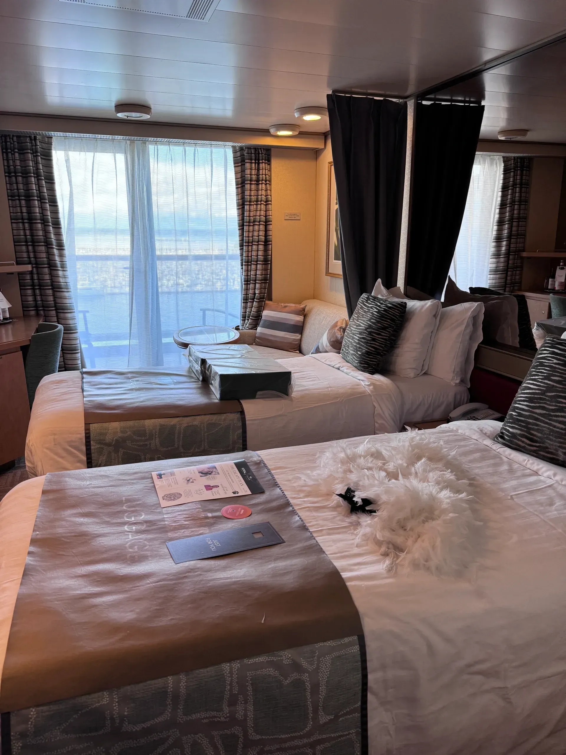 Hotel room with two neatly made beds, large window, and dark curtains.