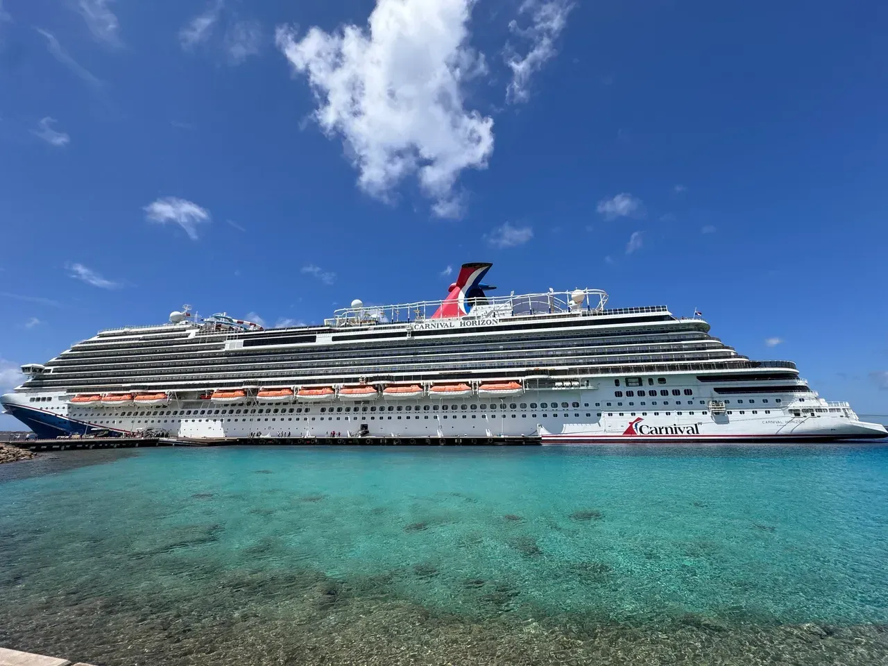 Large cruise ship on turquoise water under a bright blue sky with scattered clouds.