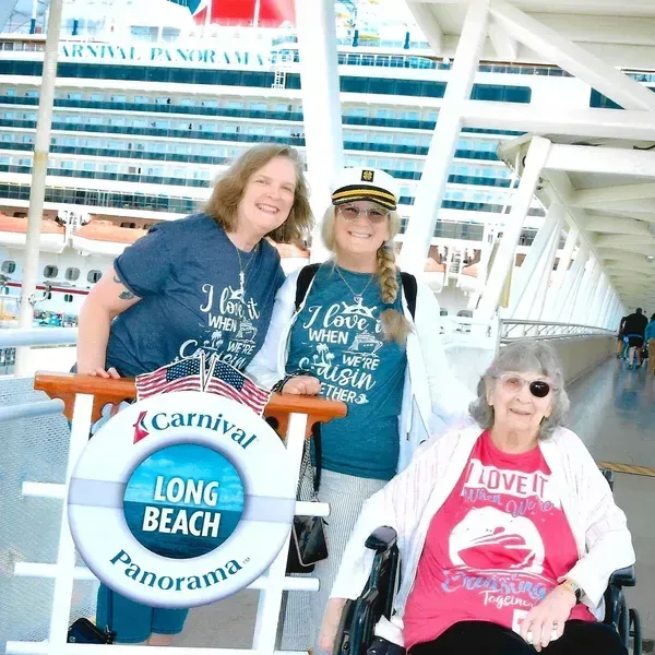 Three smiling people pose aboard a Carnival cruise ship beside a “Long Beach Panorama” sign.