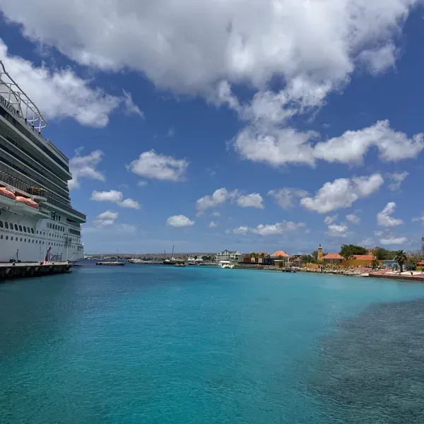 Cruise ship beside a turquoise harbor under a bright blue sky with scattered clouds.