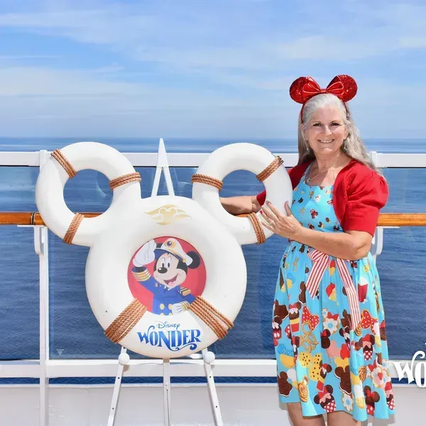 Woman in red and blue dress posing by a Mickey Mouse cruise display on a ship deck