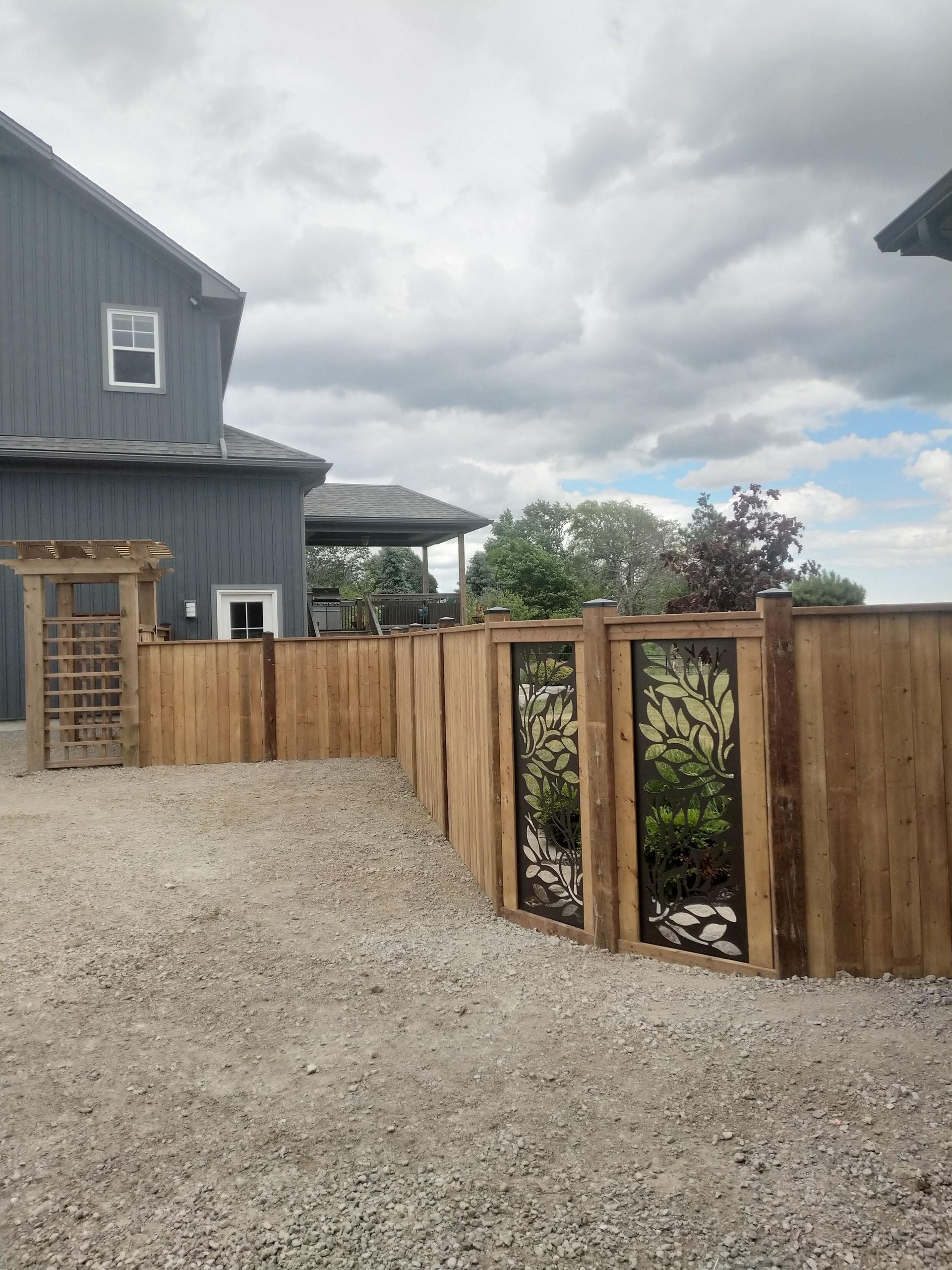 Wooden fence curves around a gravel area; a gray building is behind.