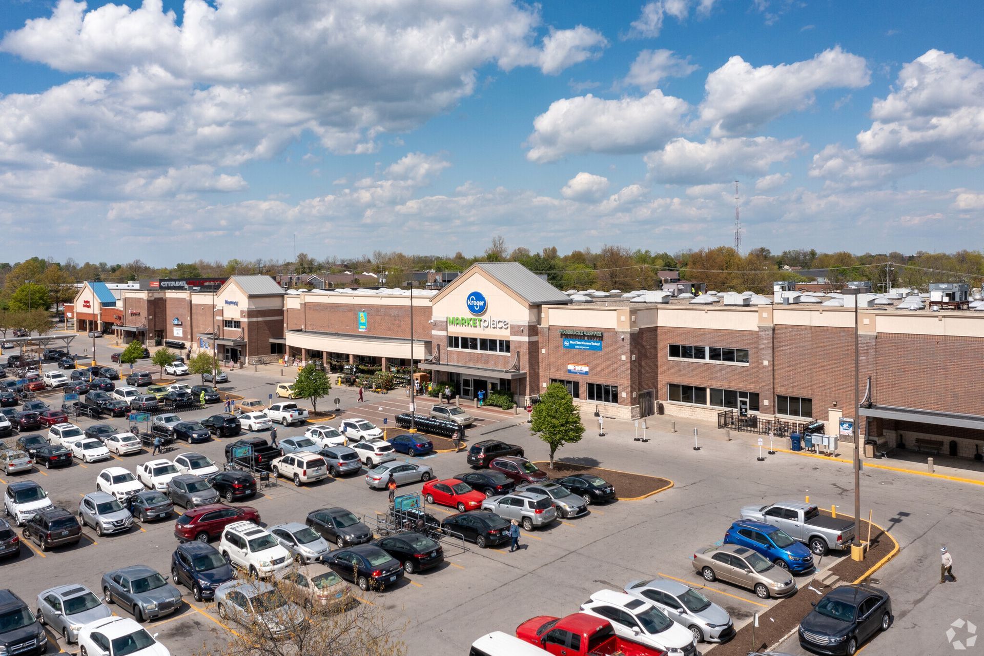 Aerial view of a busy shopping center parking lot under a partly cloudy sky