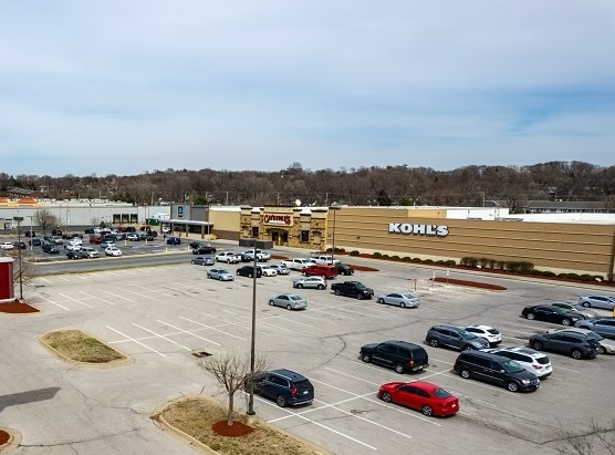 Aerial view of a busy shopping center with parking lots, storefronts, and surrounding trees