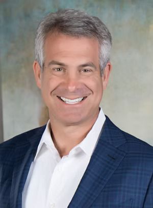 Smiling professional in a navy blazer and white shirt against a neutral backdrop