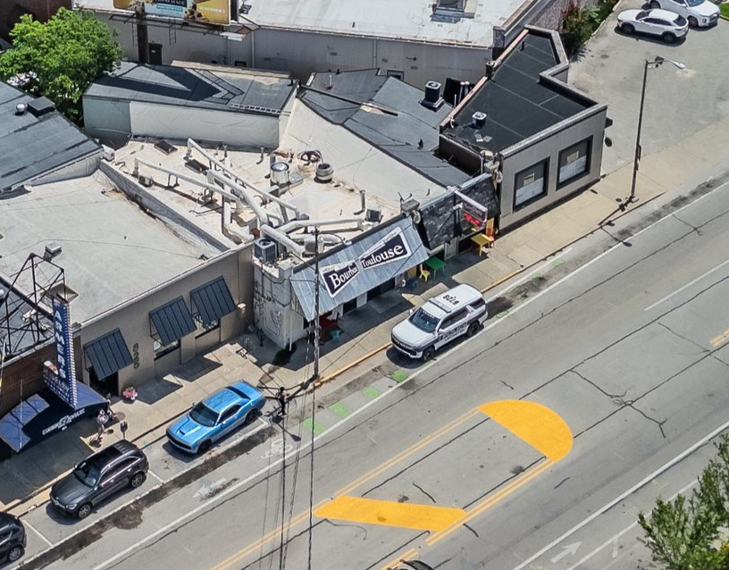 Aerial view of buildings along a road, with parked cars and a yellow painted crosswalk or lane marking