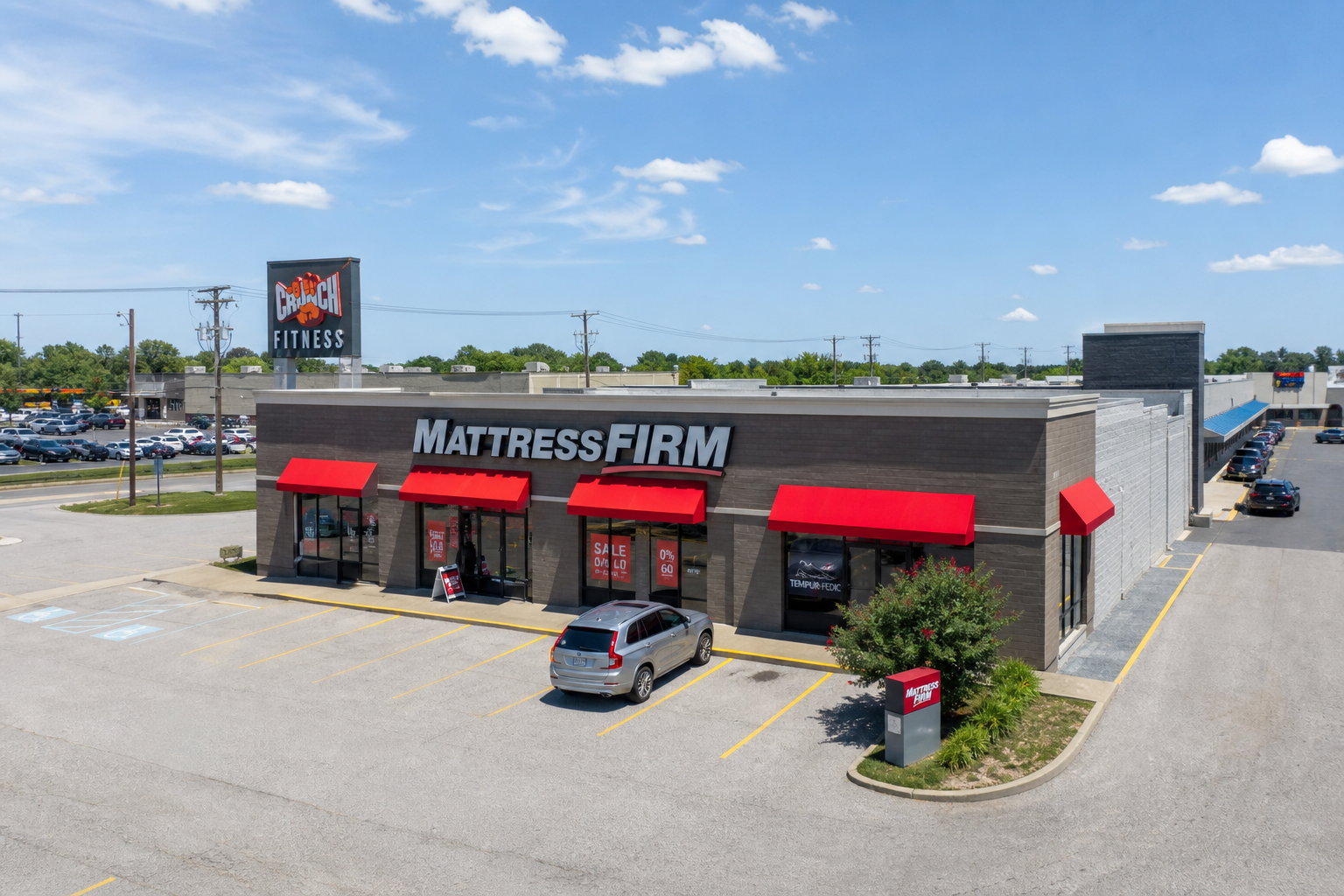 Aerial view of a shopping plaza with parking lots, storefronts, and cars along the road.