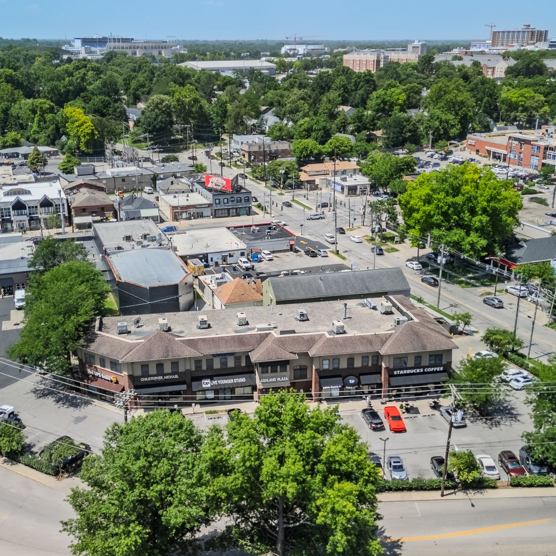 Aerial view of a residential neighborhood with trees, low-rise buildings, and parked cars.