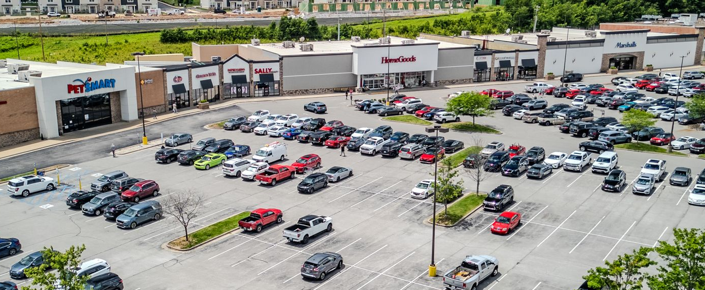 Aerial view of a strip mall with parked cars and trees along the street.