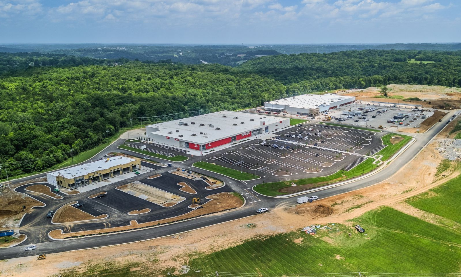 Aerial view of a large construction site with parking lots, buildings, and surrounding forest.