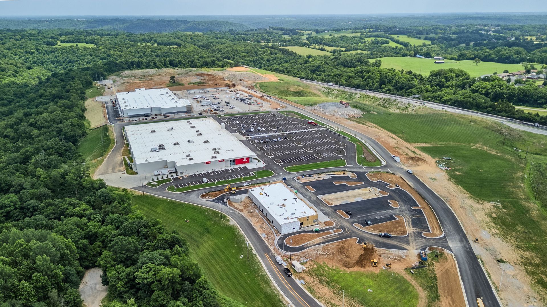 Aerial view of a large construction site with buildings, paved roads, and surrounding green fields.