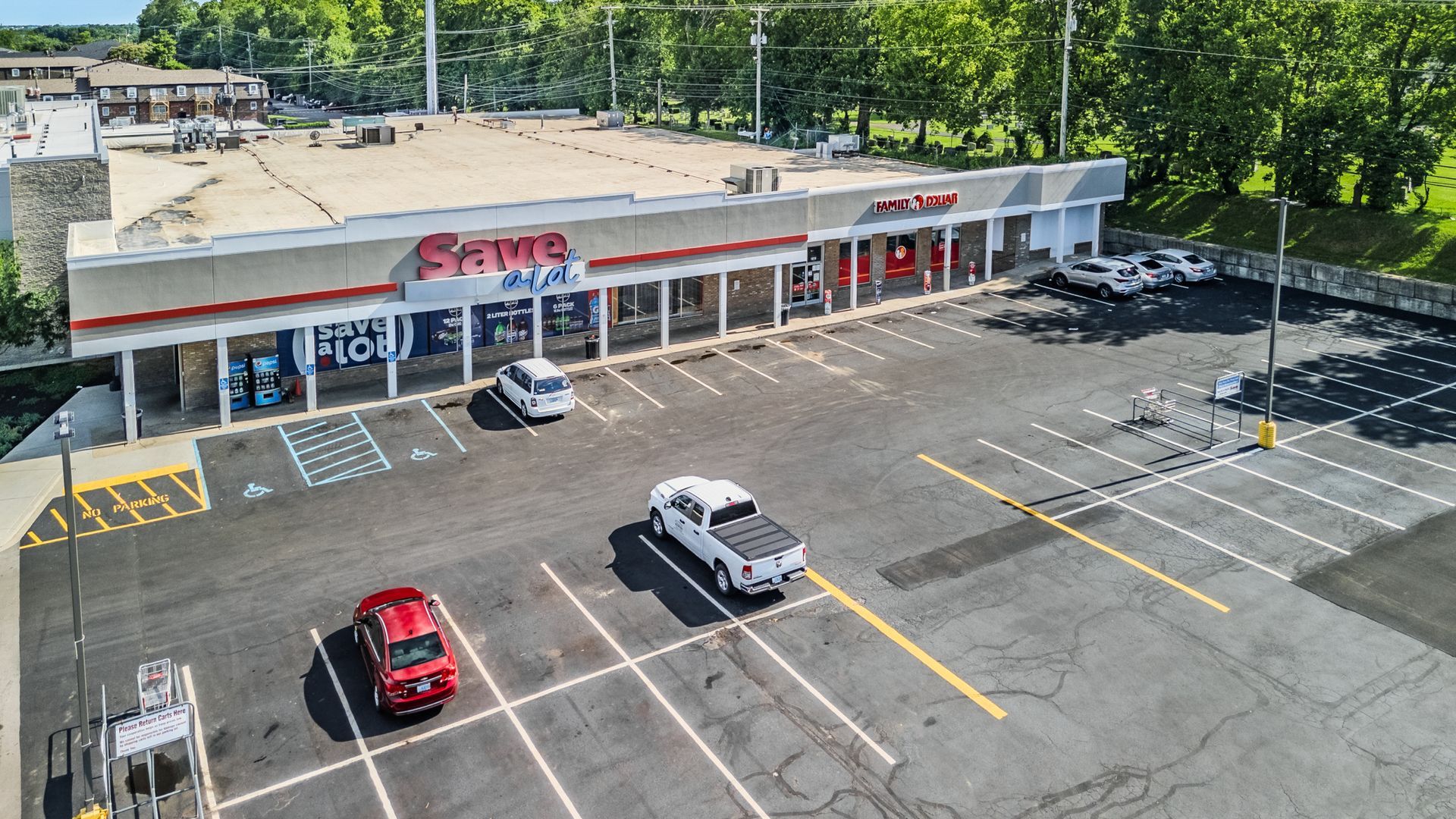Aerial view of a busy shopping center with parking lots, storefronts, and surrounding trees