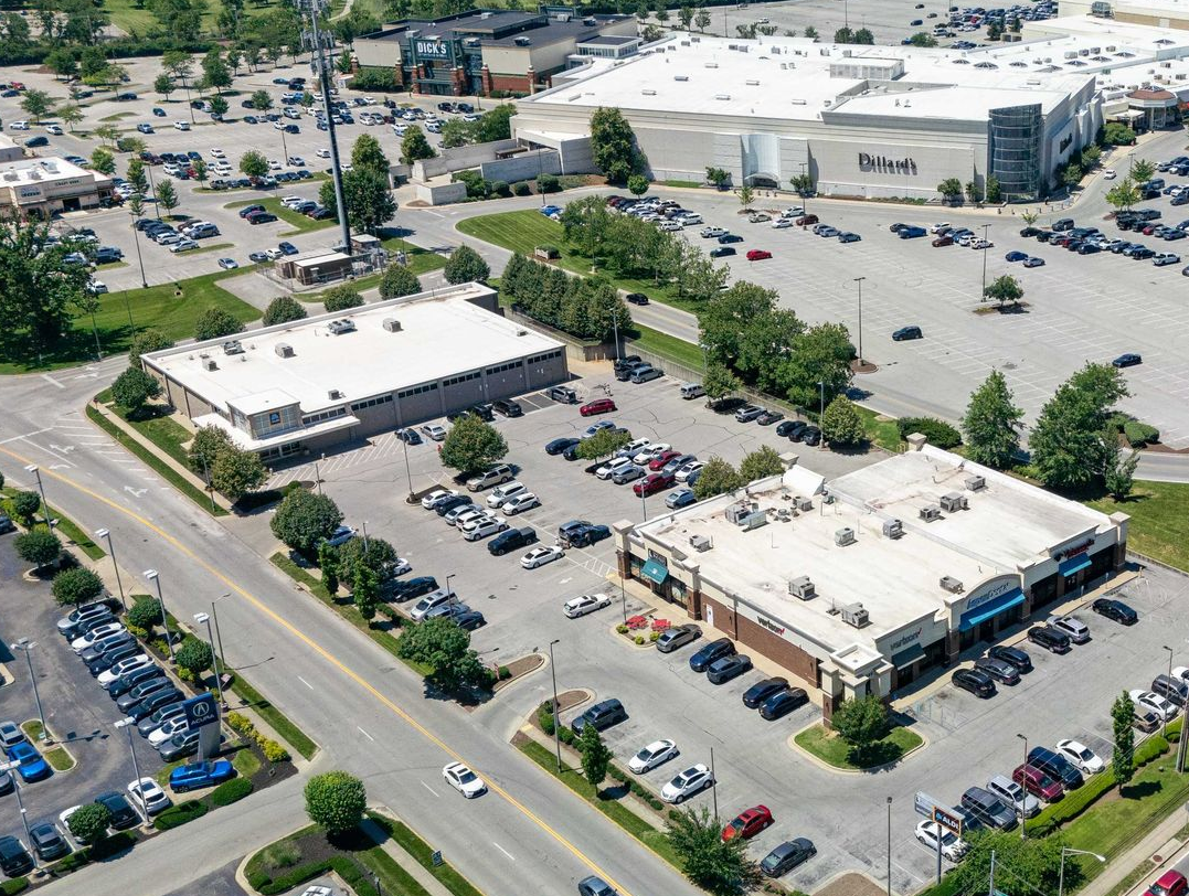 Aerial view of a large shopping center and parking lots beside a busy road.