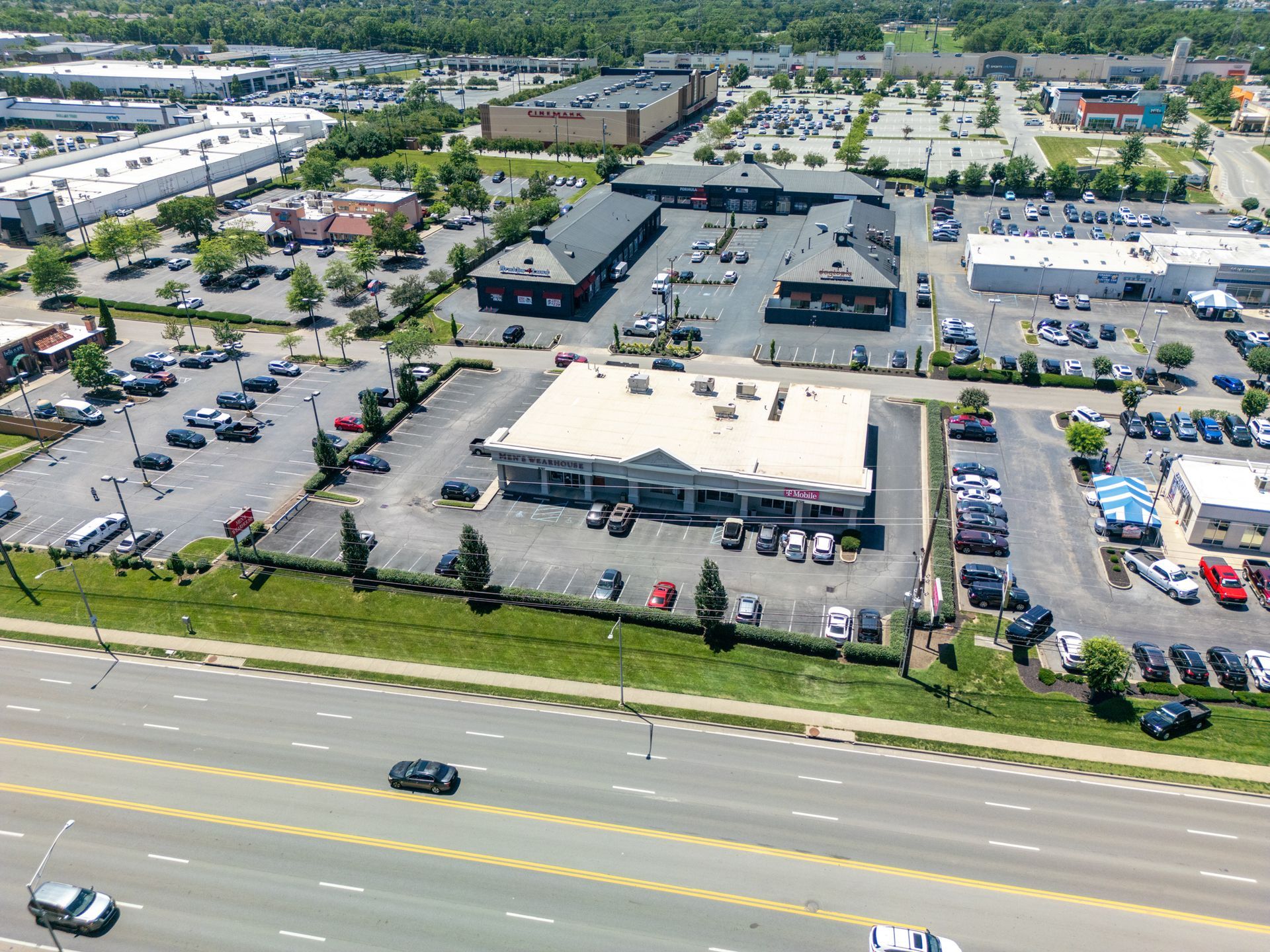 Aerial view of a busy shopping center with parked cars, stores, and tree-lined streets.
