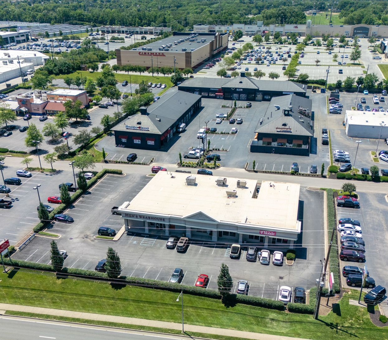 Aerial view of a commercial strip mall with parking lots and surrounding trees.