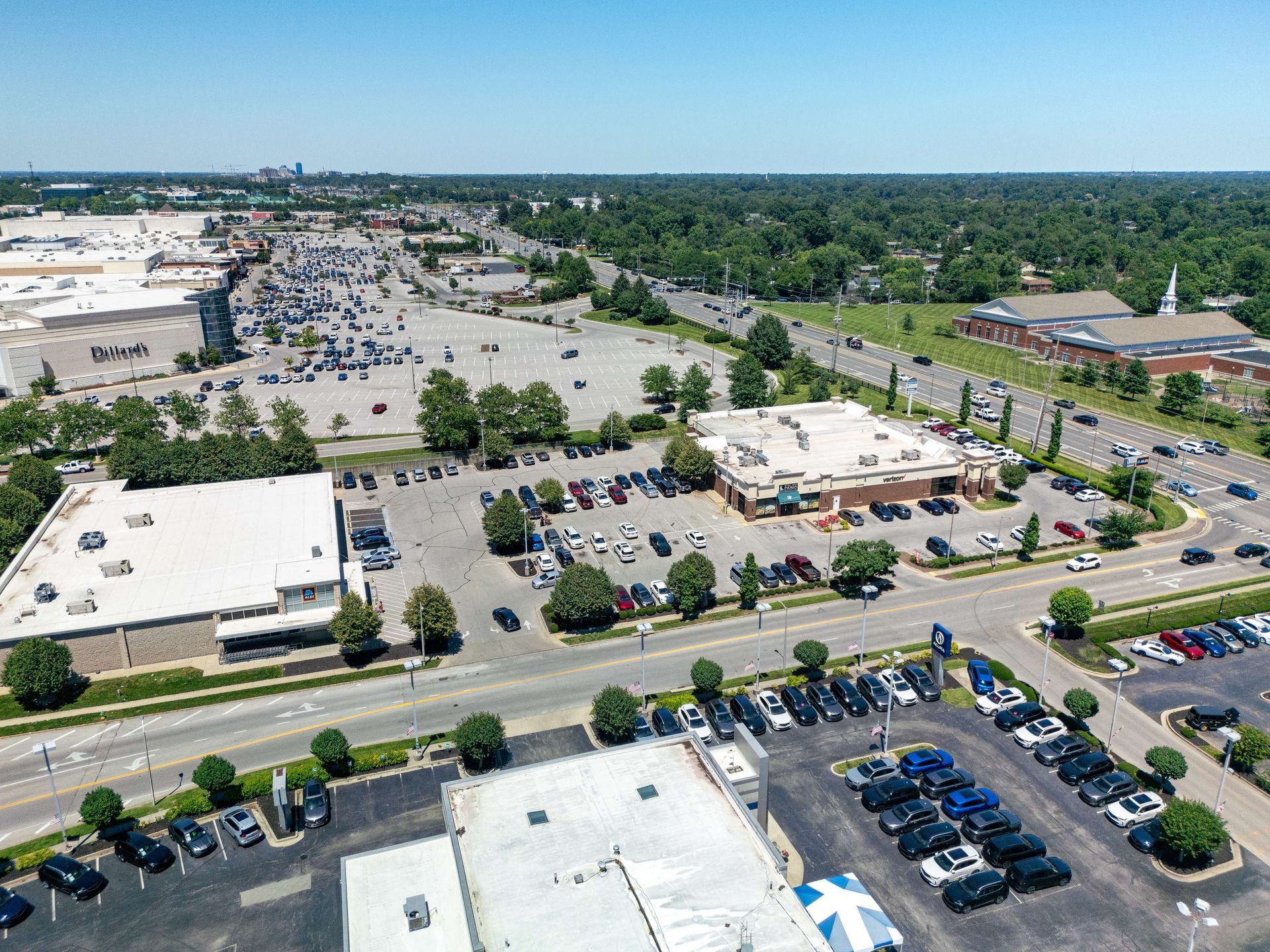 Aerial view of a shopping center parking lot with many cars and surrounding stores.