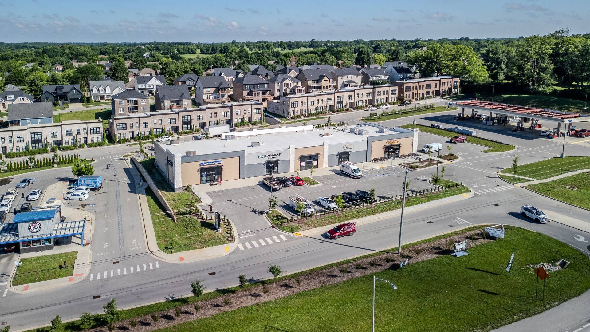 Aerial view of a busy commercial strip with storefronts, parking lots, and trees along a road