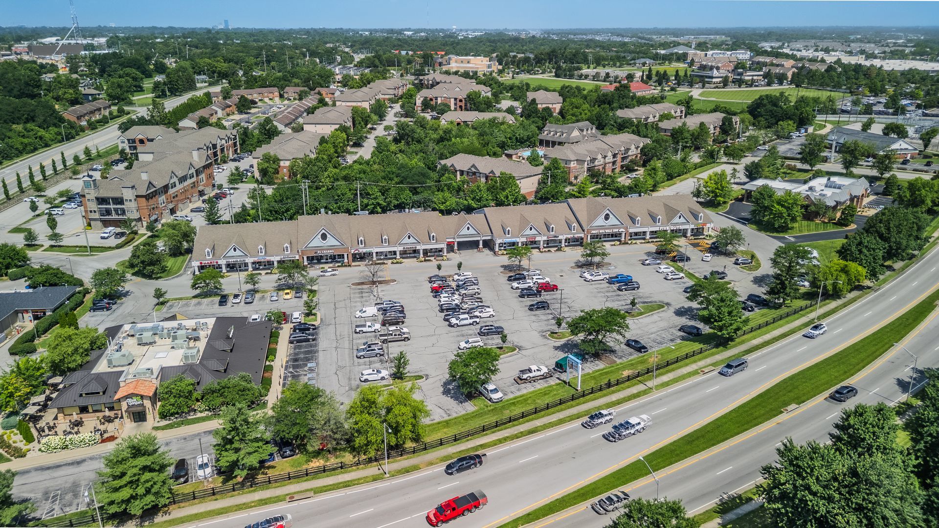 Aerial view of a busy commercial strip with storefronts, parking lots, and trees along a road