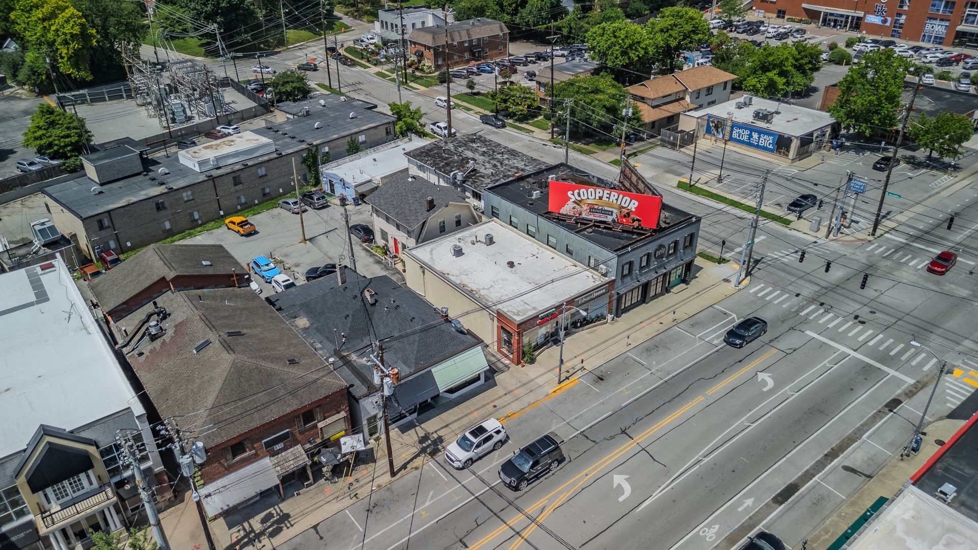Aerial view of a city intersection with cars, buildings, sidewalks, and a red-roofed storefront.