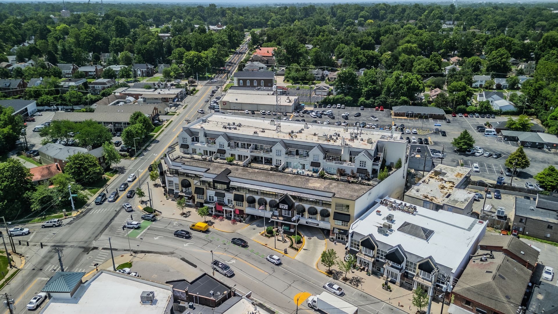 Aerial view of a busy shopping plaza with parked cars, surrounded by roads and trees.