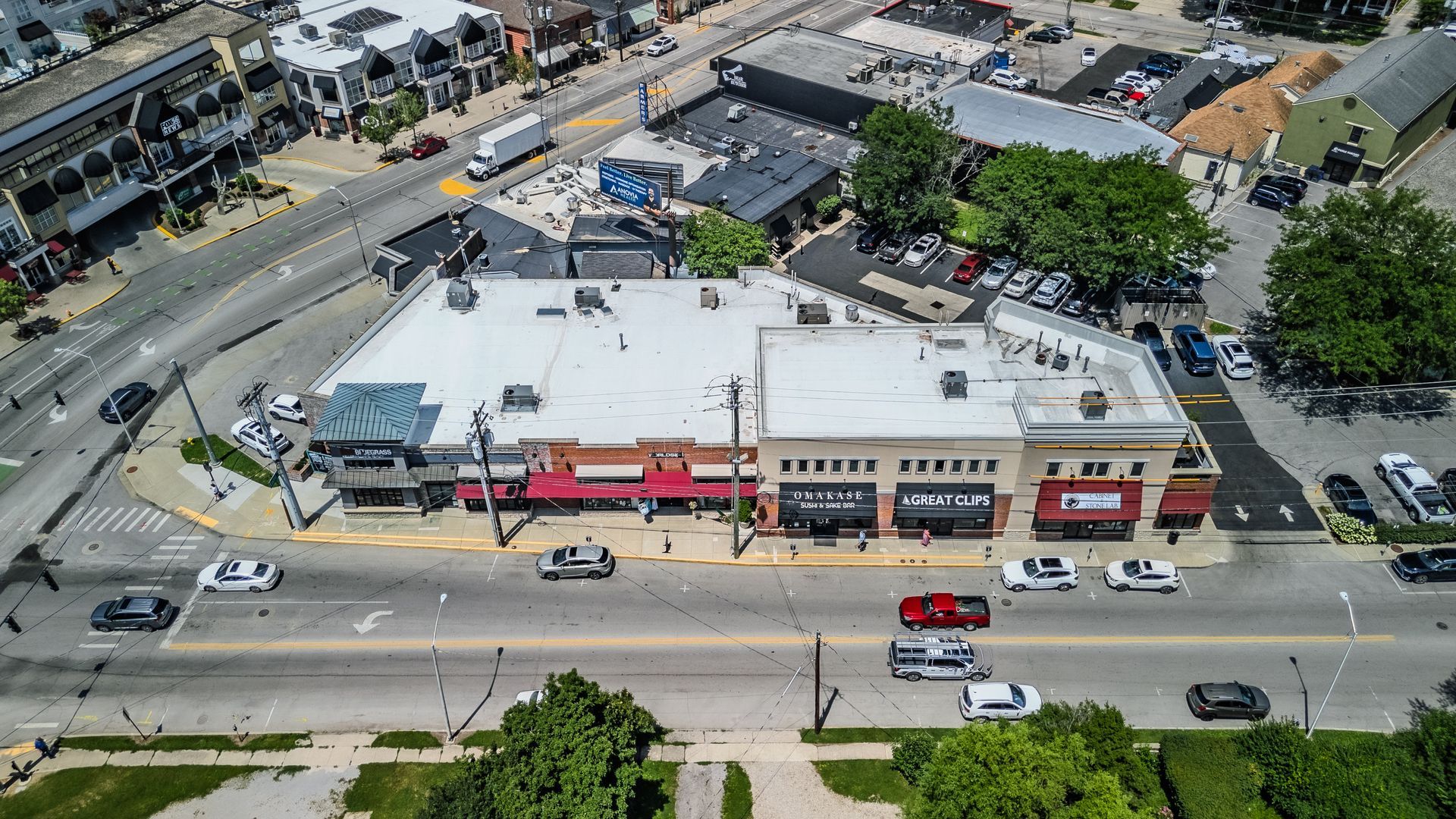 Aerial view of a busy shopping center with parking lots, storefronts, and surrounding trees