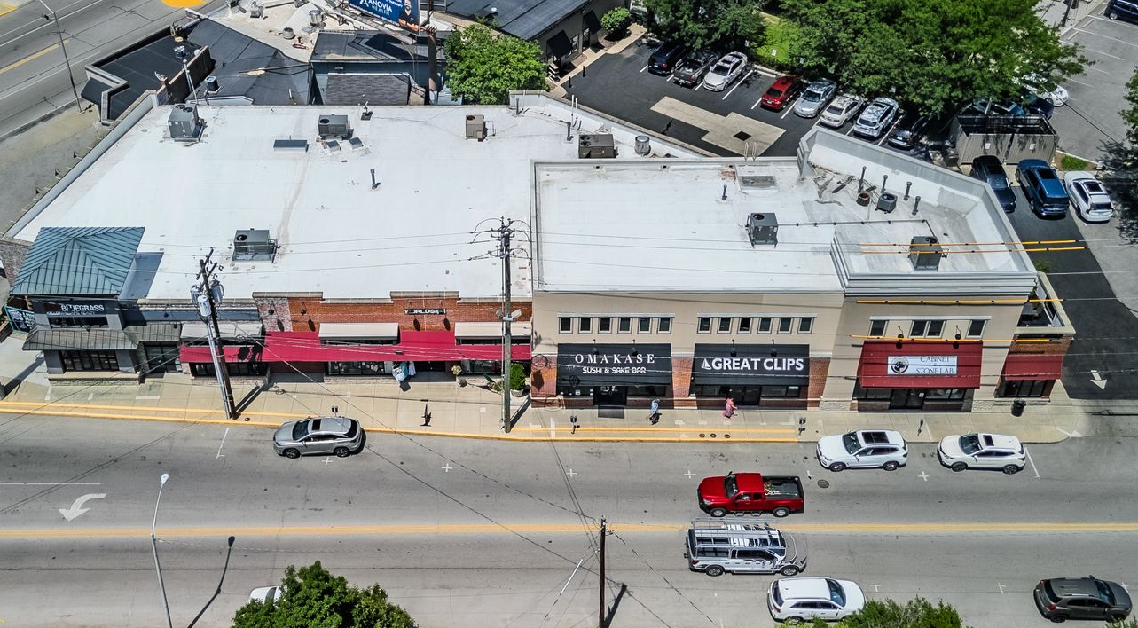 Aerial view of a row of shops with parked cars and traffic on a street below.