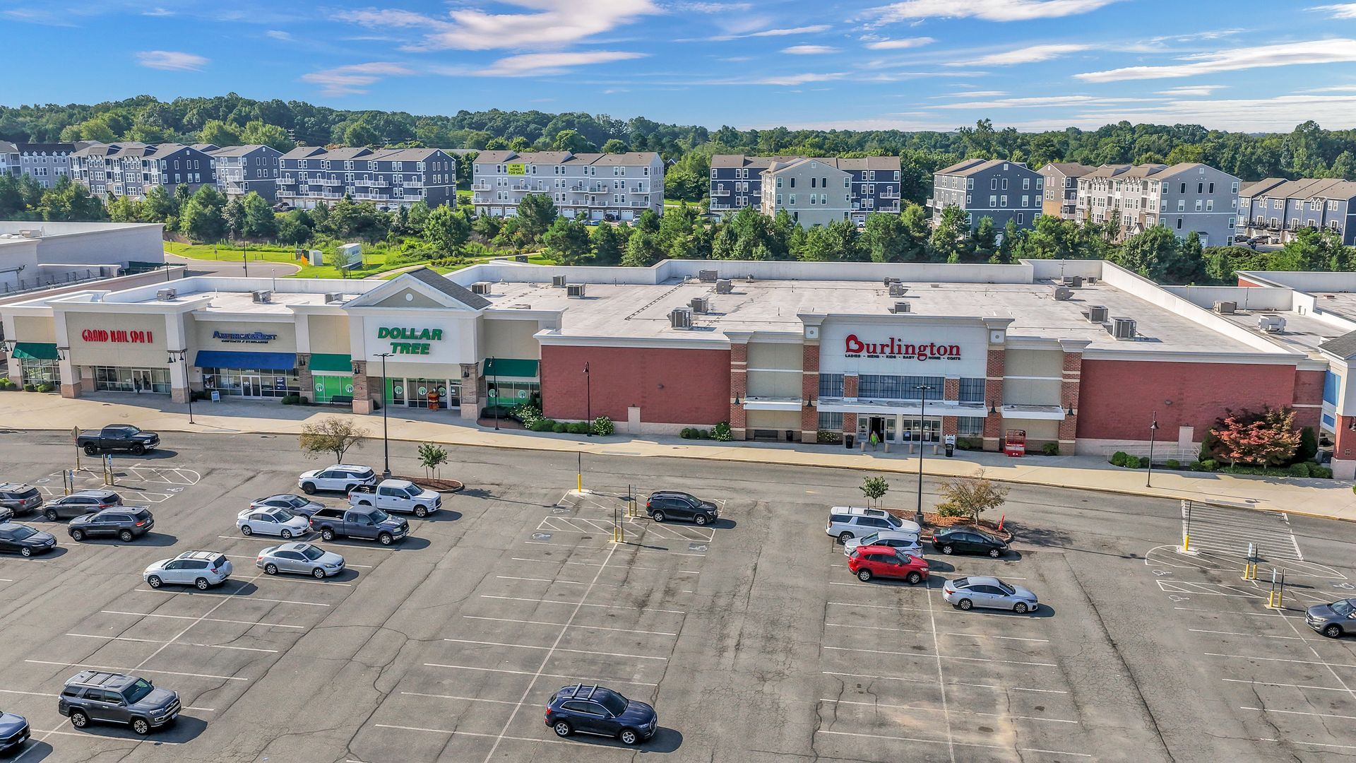 Aerial view of a busy shopping center with parking lots, storefronts, and surrounding trees
