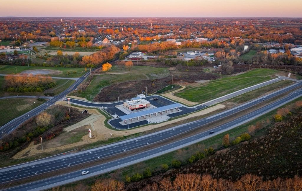 Aerial view of a highway interchange beside a white building and autumn trees at sunset.