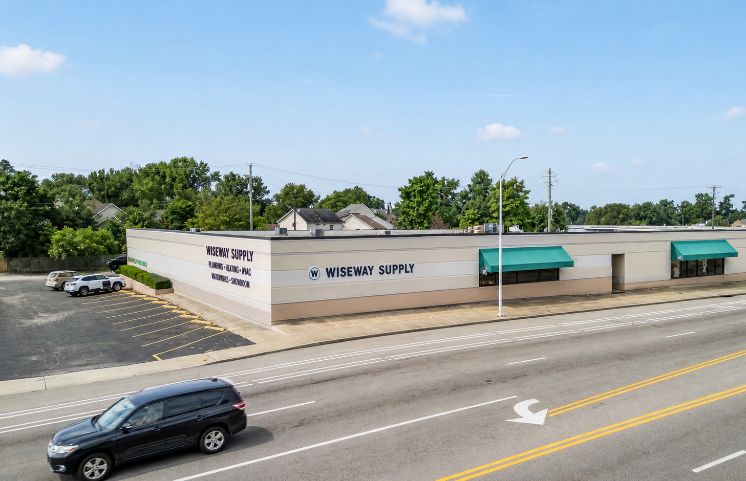 Cars waiting at a green-roof gas station with bushes and a grassy median in front