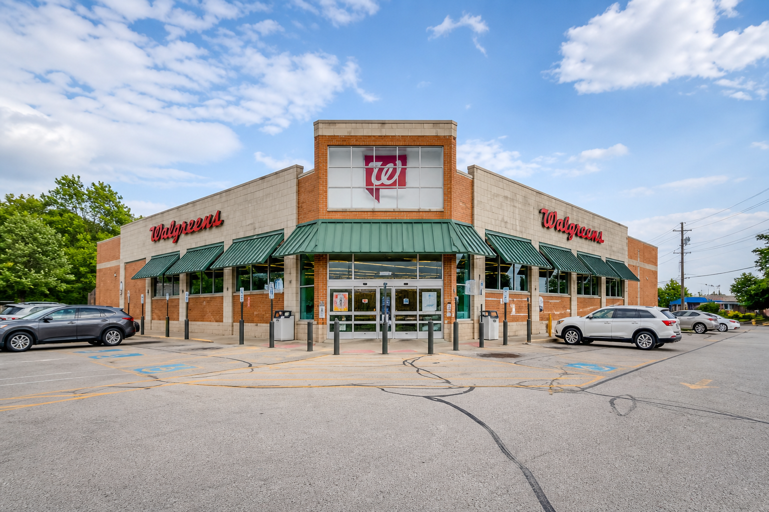 Shopping plaza exterior with storefronts, parked white SUV, and a red sign under a covered walkway