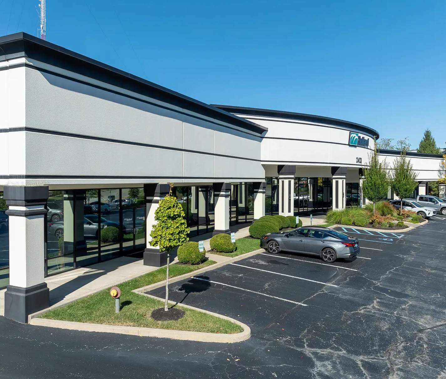 Modern office building with glass windows and a mostly empty parking lot on a sunny day