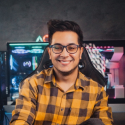 Um homem usando óculos e uma camisa xadrez está sentado em frente a um monitor de computador