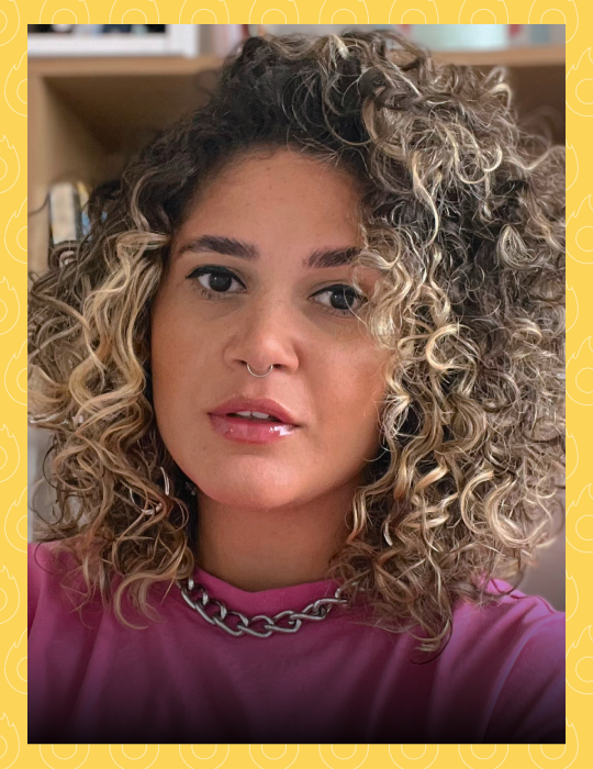 Uma mulher com cabelos cacheados está vestindo uma blusa roxa e um colar.