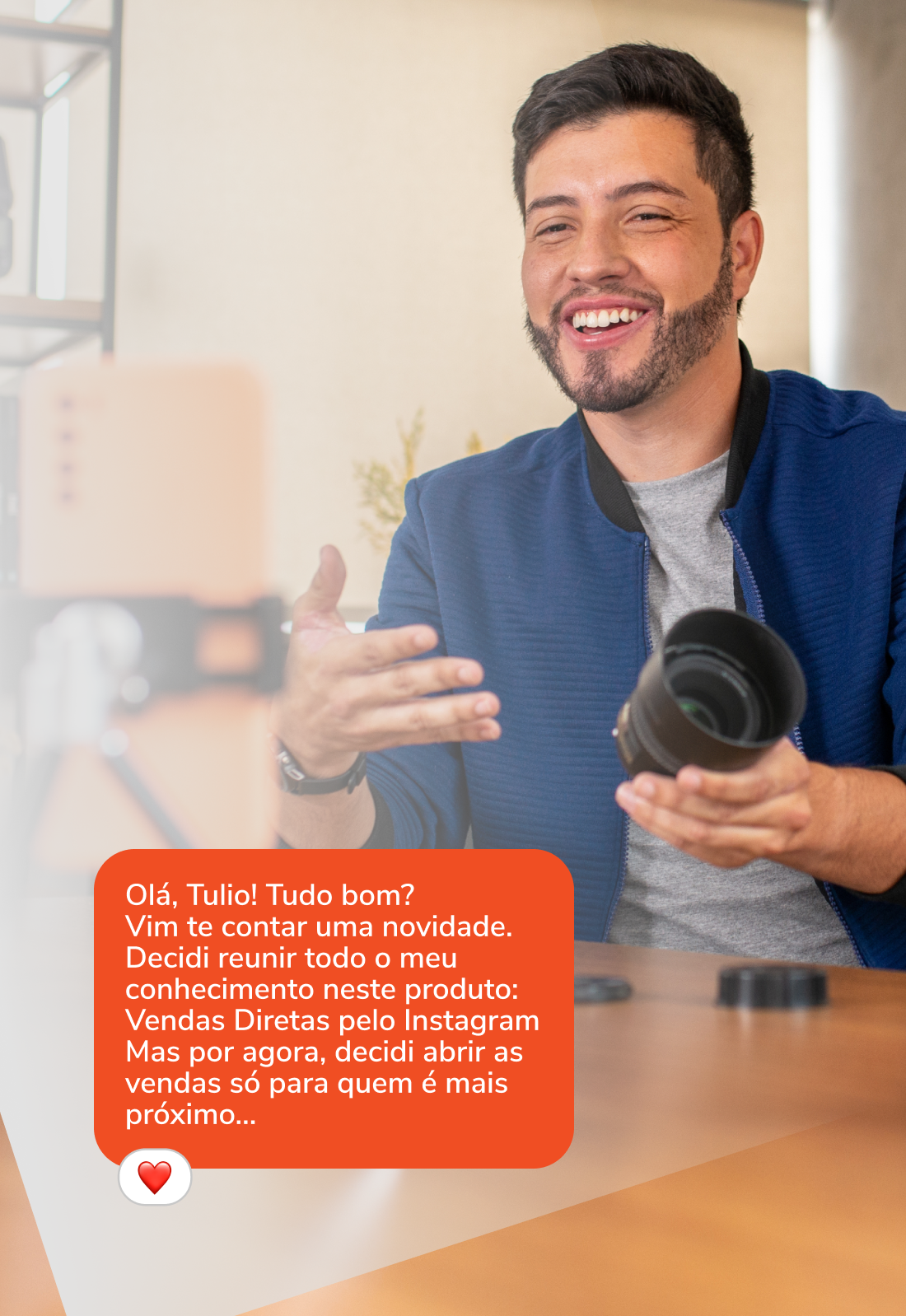 Um homem está sentado à mesa segurando uma câmera e sorrindo.
