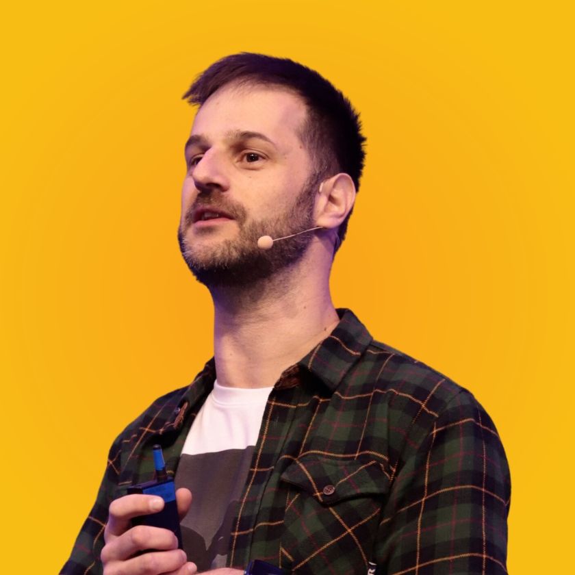 Um homem com barba vestindo uma camisa xadrez e um microfone