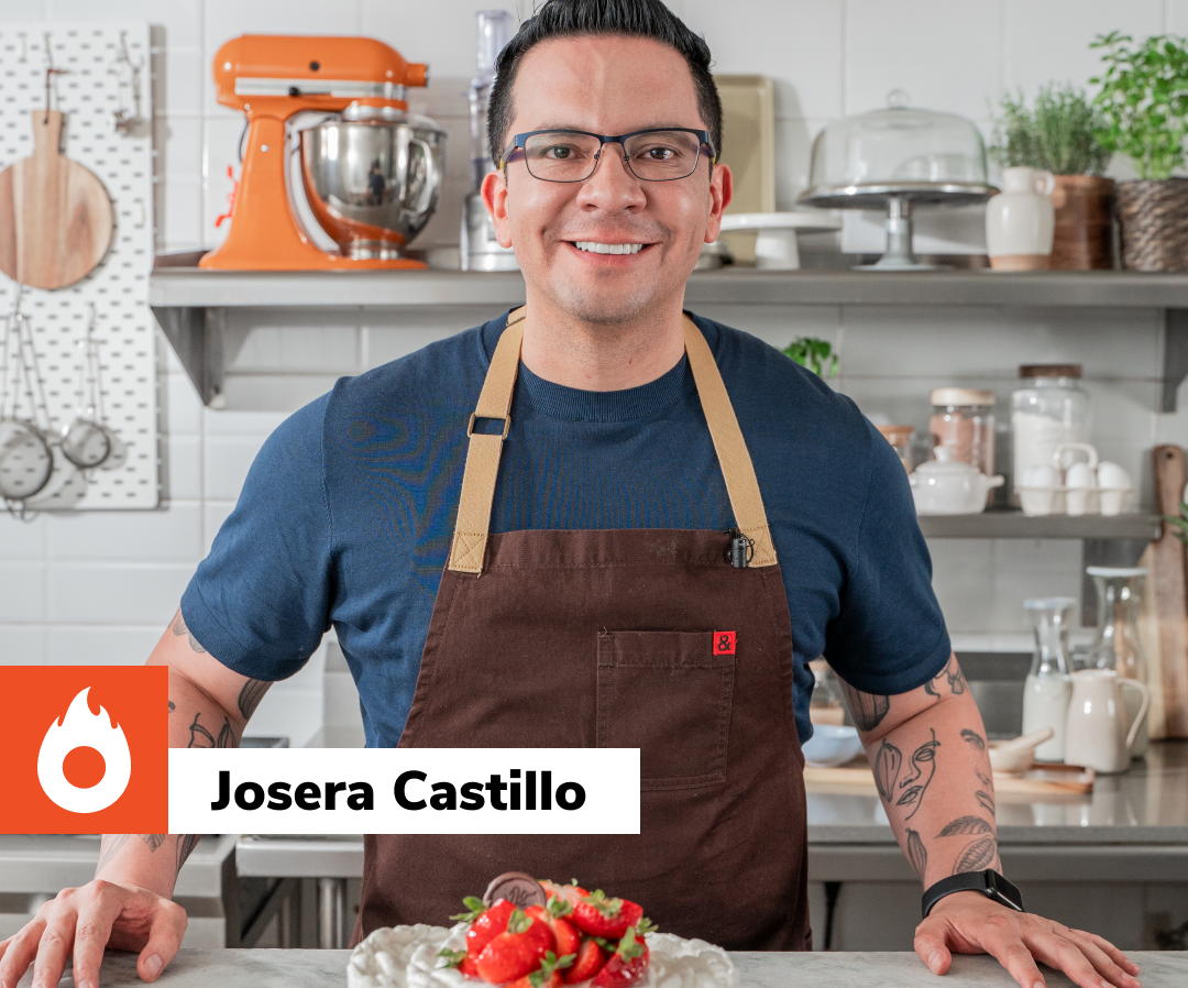 Um homem de avental está de pé na cozinha ao lado de um bolo com morangos.